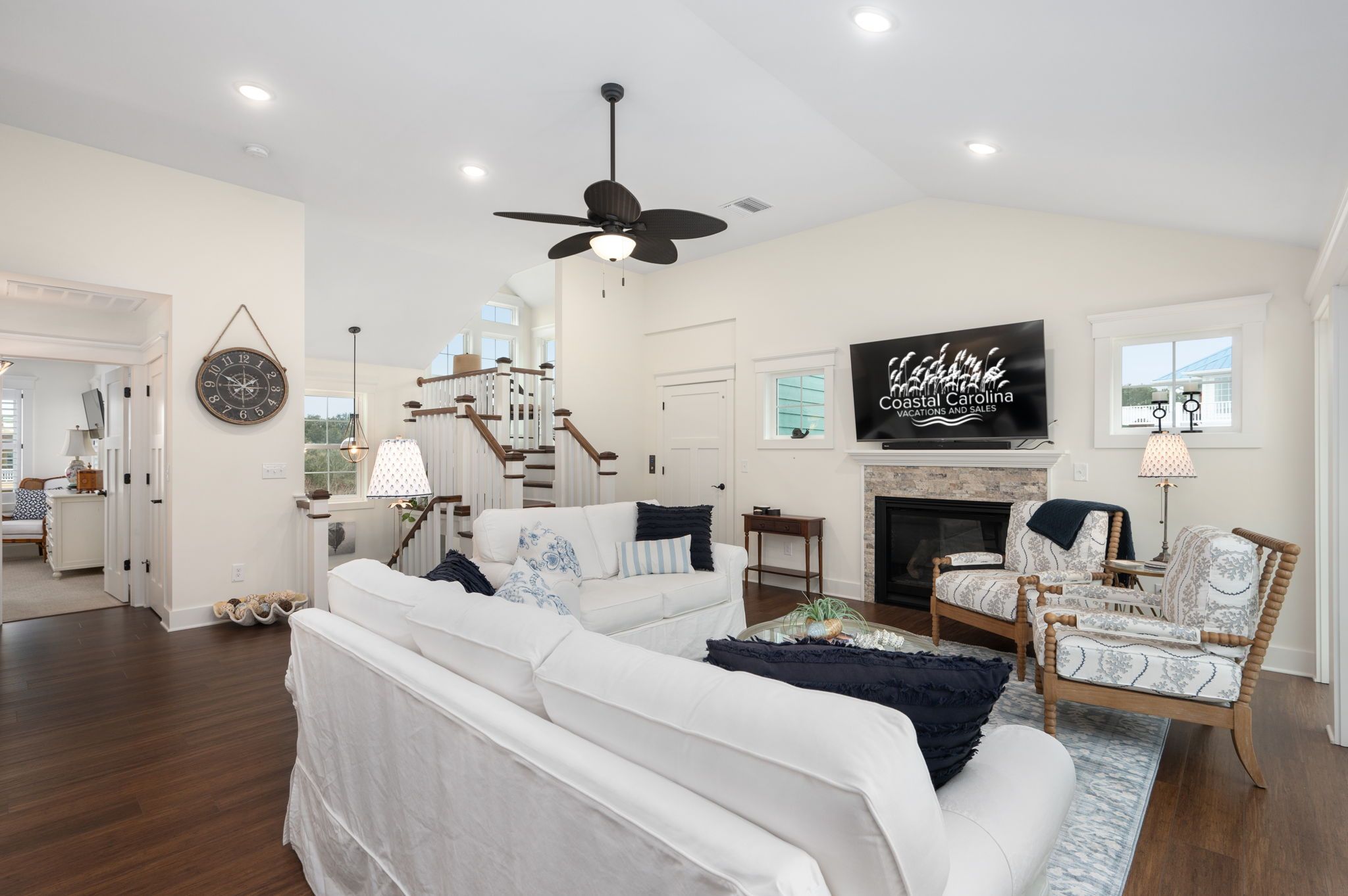 A spacious living room with a white sofa, a fireplace, and a television displaying 'Coastal Carolina Vacations and Sales'.