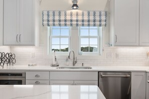 Una cocina moderna con armarios blancos, un lavamanos de acero inoxidable y una ventana con un valance estampado.