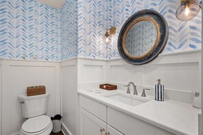 A bathroom with a white toilet, a white sink with a silver faucet, a mirror with a gold frame, and a patterned wallpaper.
