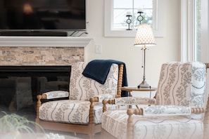 A living room with a fireplace, patterned armchairs, a side table, and a lamp. - Between the Cs: Soundside, Private Pool, Elevator (Kitty Hawk)