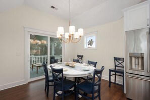 A dining area with a round table, dark chairs, a chandelier, and a stainless steel refrigerator.