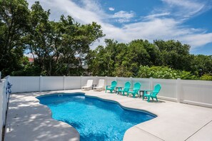 A swimming pool with a curved edge, surrounded by a white fence and trees.