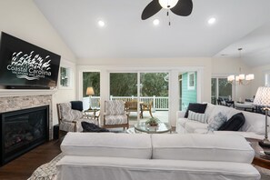A spacious living room with a fireplace, comfortable seating, and a television displaying 'Coastal Carolina Vacations and Sales'. - Between the Cs: Soundside, Private Pool, Elevator (Kitty Hawk)