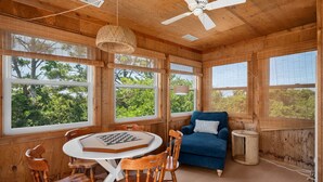 A wooden interior with a ceiling fan, large windows, a blue sofa, and a chessboard on a table.