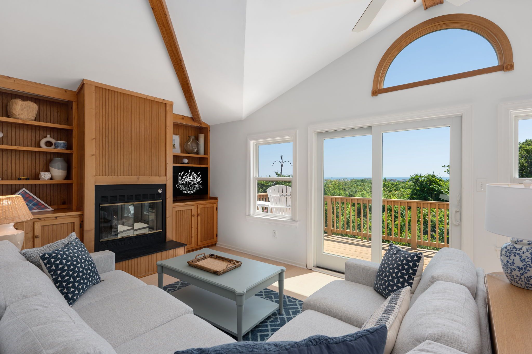 A spacious living room with a fireplace, wooden shelves, and a balcony with a view.