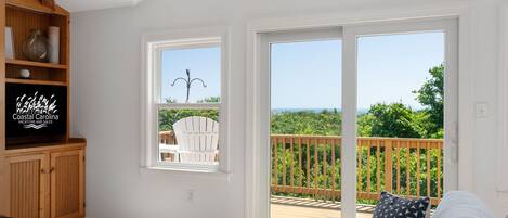 A spacious living area with a large sliding glass door leading to a deck with a view of the ocean.
