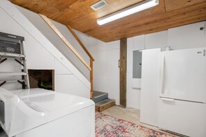 Uma cozinha com eletrodomésticos brancos, escada de madeira e tapete estampado.