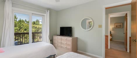 A bedroom with two beds, a TV, a dresser, and a balcony with curtains.