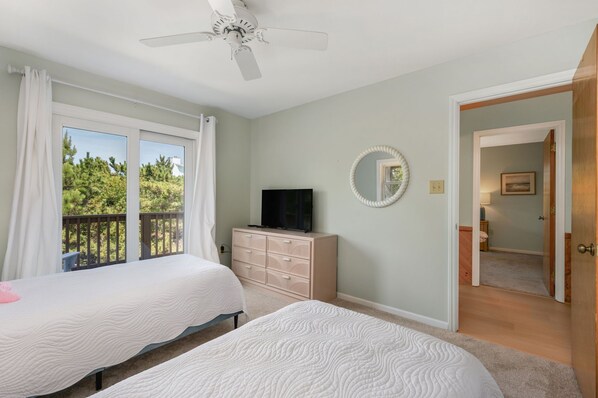 A bedroom with two beds, a TV, a dresser, and a balcony with curtains.