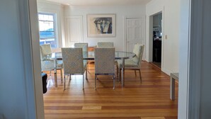A dining area with a glass table and patterned chairs, wooden flooring, and a ceiling fan.
