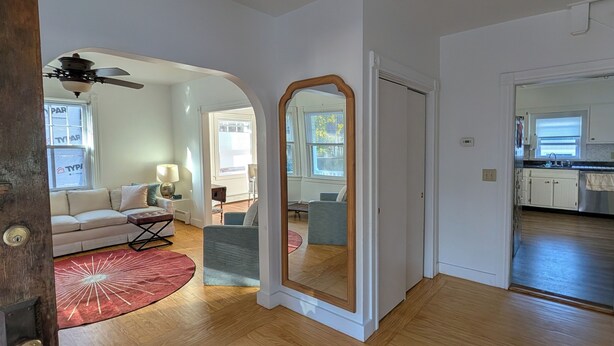 A spacious living area with a wooden floor, a red rug, a ceiling fan, and a large mirror.