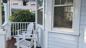 A white porch with wooden flooring, white railings, and a large window.