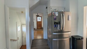 A kitchen with a stainless steel refrigerator, wooden flooring, and white walls.