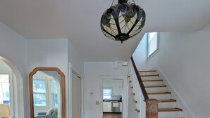 A spacious hallway with wooden flooring, a staircase with wooden steps and a wooden handrail, and a large mirror on the left wall.