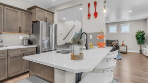 A modern kitchen with a large island, stainless steel appliances, and a dining area with a bar stool.