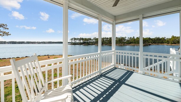 A covered porch with white railings, a ceiling fan, and a view of a lake and trees. - Carolina Breeze - Your Perfect Getaway! (Merritt)