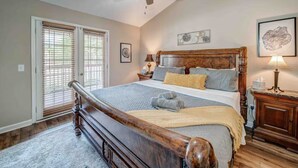 Una camera da letto con un letto grande, una testiera in legno, una ventola a soffitto, un comodino con una lampada e una finestra con persiane.