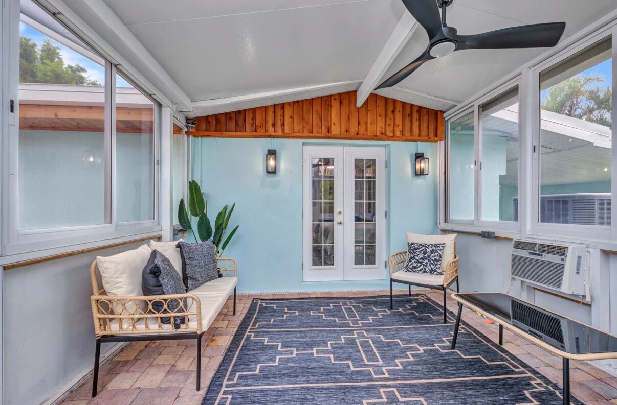 A covered patio with a ceiling fan, a rattan sofa, a patterned rug, and a view through the glass doors.