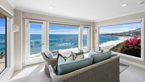 Een ruim balkon met uitzicht op de oceaan, rieten meubels en een glazen tafel.