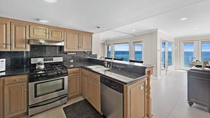 Een moderne keuken met roestvrijstalen apparatuur, houten kastjes en uitzicht op de oceaan door grote ramen.
