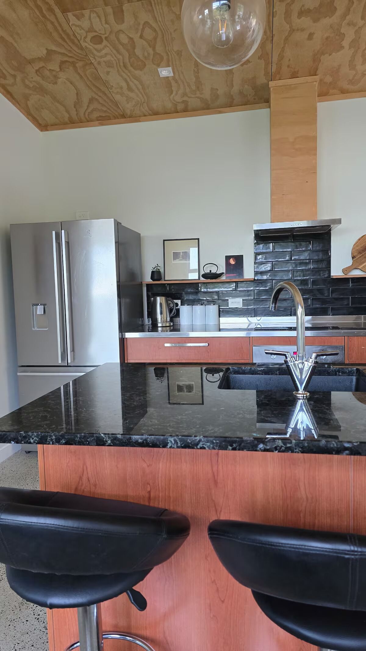 Cozinha moderna com bancada de granito, eletrodomésticos de aço inoxidável e painel de parede preto.