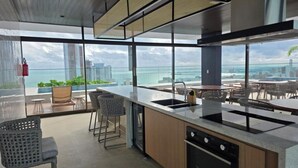 A modern kitchen with a large island, a sink, and a view of the city and ocean. - New High Standard Studio Fortaleza • Beach 200 m (Meireles Fortaleza)