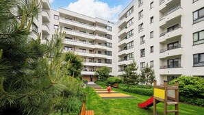 A multi-story residential building with balconies, a grassy courtyard, and a children's play area. - Włochy Równoległa Cosy Apartment (Warszawa)