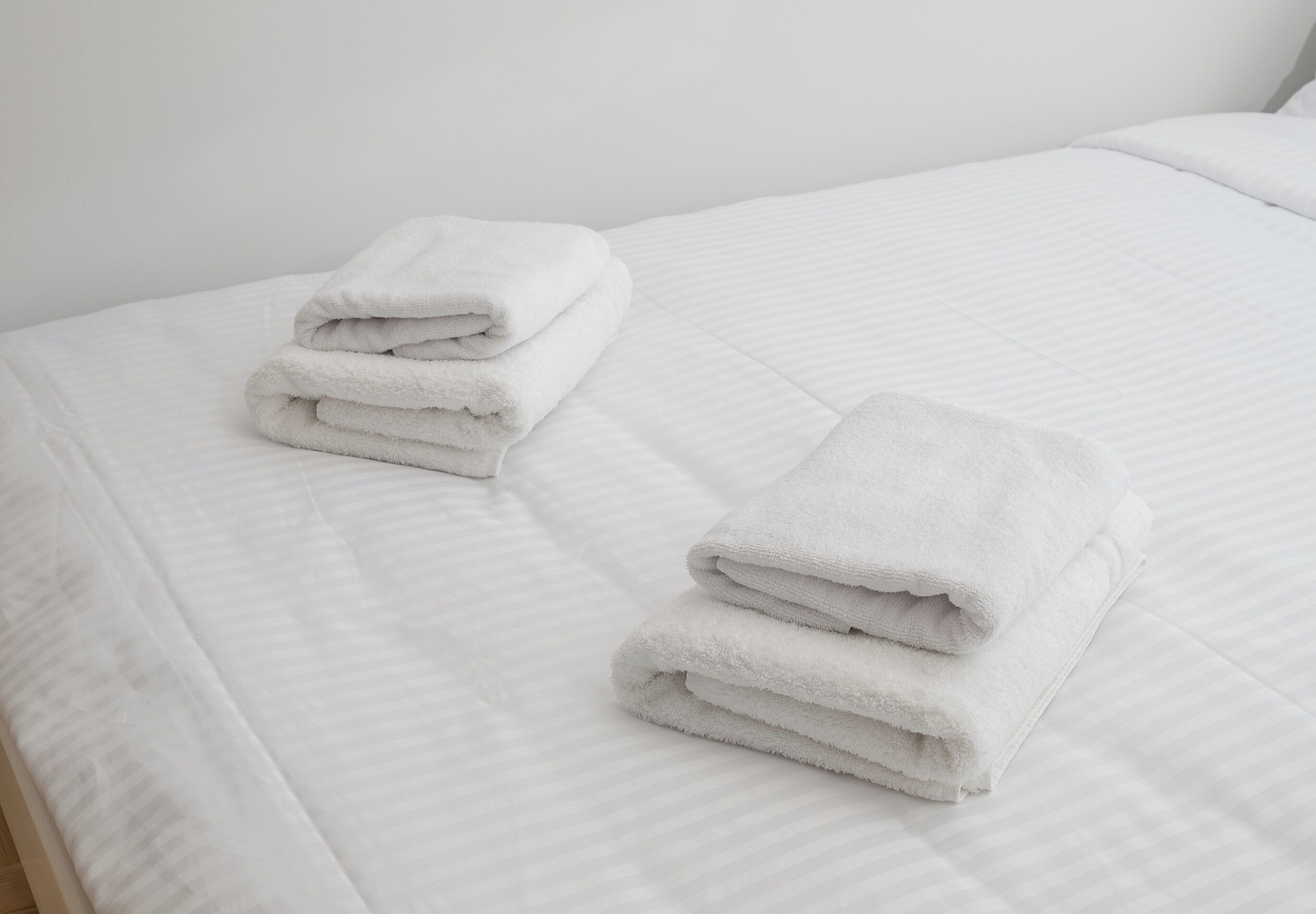 A neatly made bed with white linens and a folded white towel on the side.