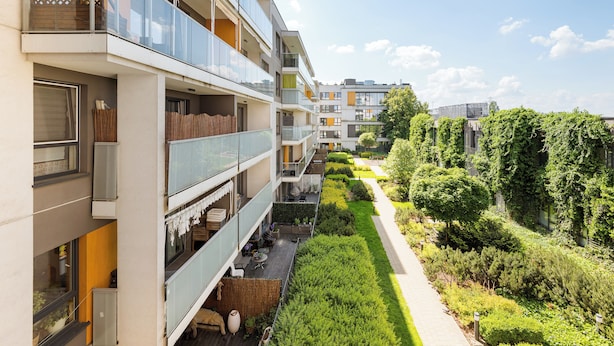 Een modern appartementencomplex met meerdere balkons, een verzorgde tuin en een heldere lucht.