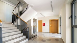 Een moderne hotellobby met een trap, lift en een gang die leidt naar een deur met het nummer 80.
