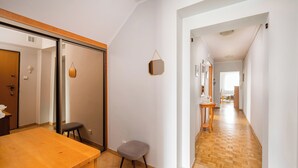 A modern interior with a wooden dining table, a small stool, and a hallway leading to another room. - National Stadium Spacious Apartment (Warszawa)