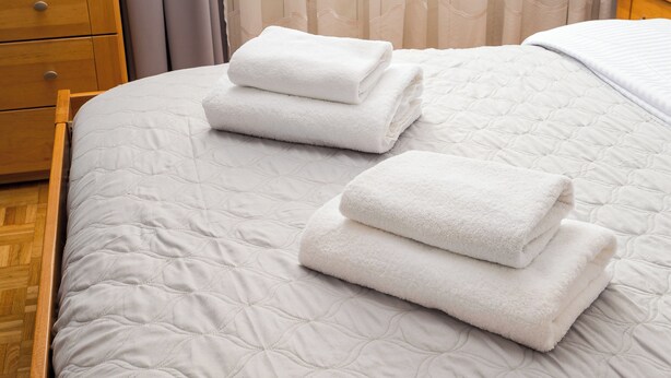 A neatly made bed with a quilted white bedspread and two folded white towels on top. - National Stadium Spacious Apartment (Warszawa)