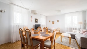 A dining area with a wooden table and chairs, a television, and a sofa in the background. - National Stadium Spacious Apartment (Warszawa)