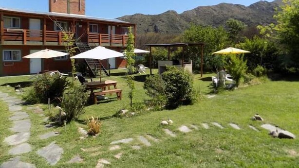 A two-story building with a patio area featuring outdoor seating and umbrellas. - Complejo Turístico Holtfor  (Potrero de los Funes)