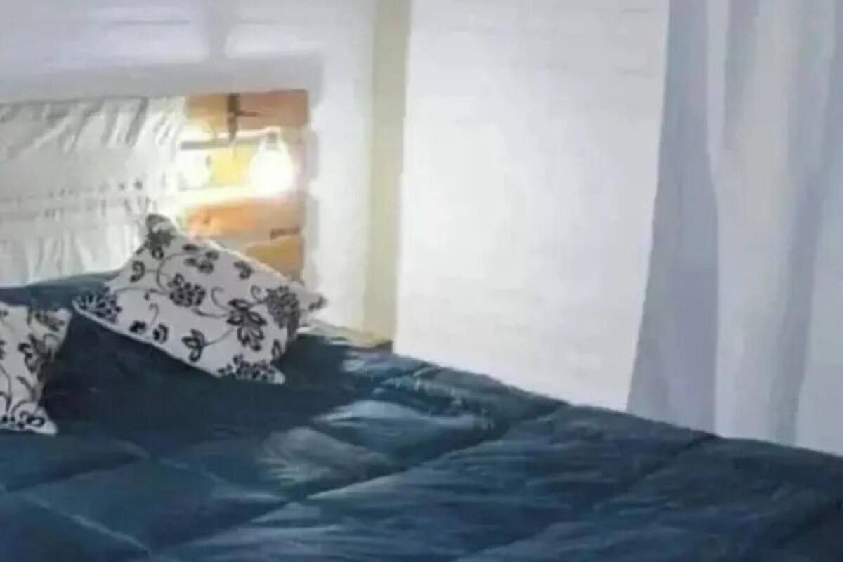 Un lit recouvert d’une couette bleu foncé et agrémenté d’oreillers à motifs, un mur en briques blanches et une fenêtre avec des rideaux.