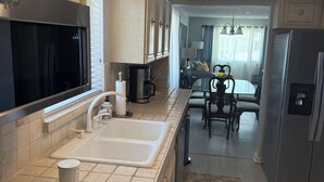 A kitchen with a double sink, a stove, a refrigerator, and a dining area with a table and chairs. - Sunsets and Palm Trees overlooking the St. Lucie River (Stuart)