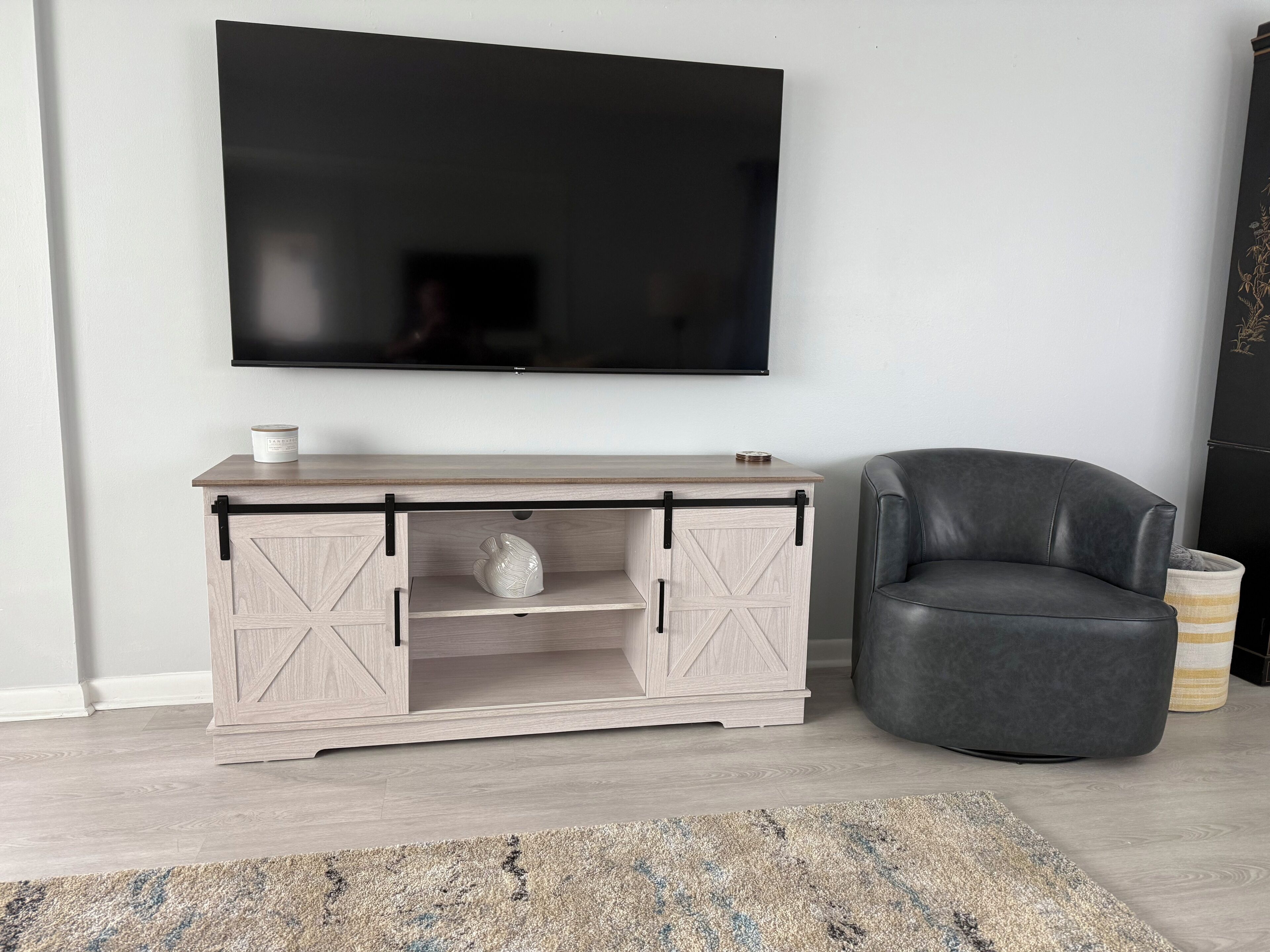 Un soggiorno moderno con una televisione a schermo piatto montata a parete, un mobiletto in legno chiaro con ante scorrevoli, una poltrona in pelle scura e un tappeto decorato sul pavimento.