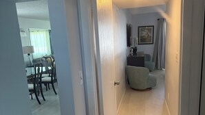 A hallway leading to a living area with a dining table and chairs, a gray sofa, and a television on the wall. - Sunsets and Palm Trees overlooking the St. Lucie River (Stuart)