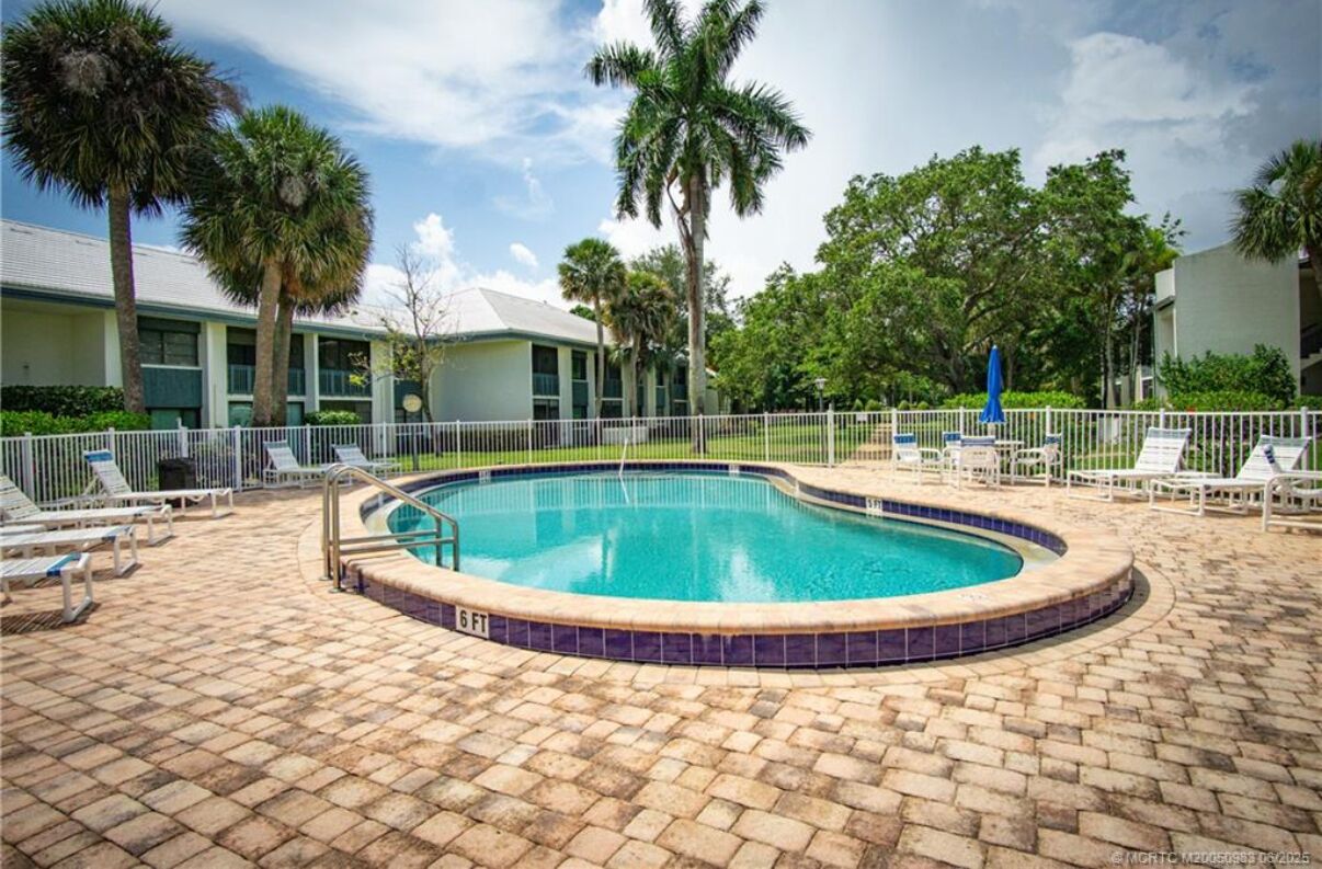 A circular pool with a tiled edge, surrounded by lounge chairs and a fence.
