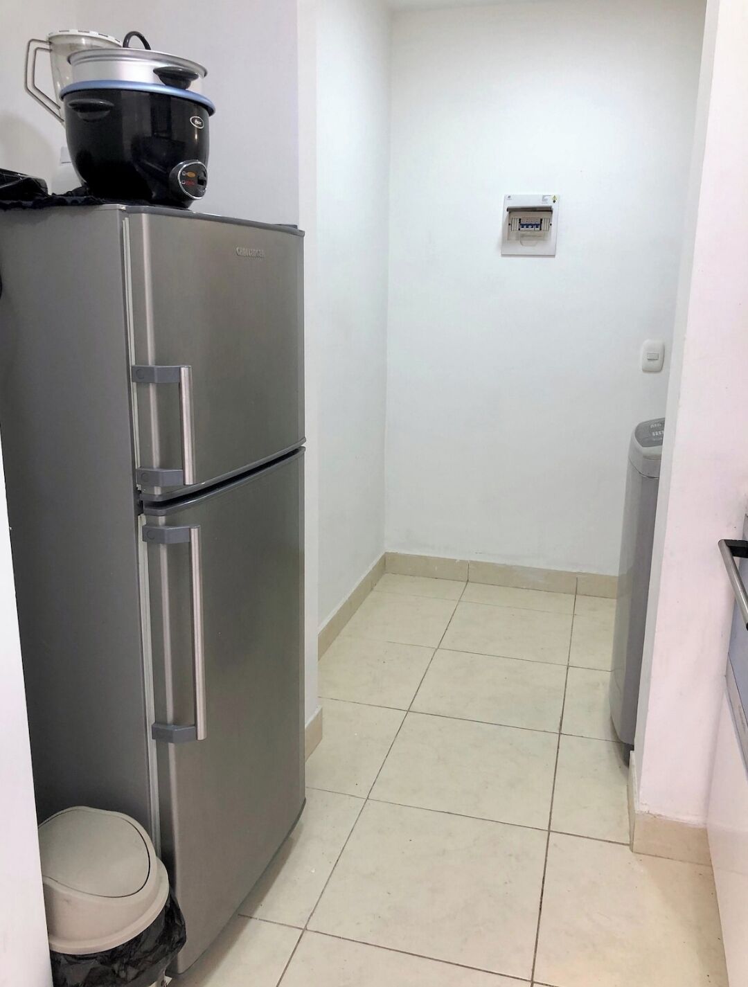 Une cuisine compacte équipée d’un réfrigérateur en acier inoxydable, d’une petite poubelle et d’une prise électrique murale.