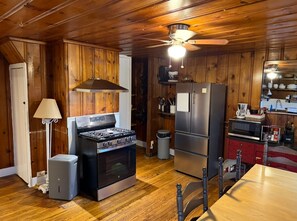 Una cocina con paredes de madera, estufa, refrigerador y una mesa de comedor.