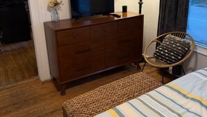 Un dormitori amb un taulell de fusta, una televisió, una làmpada, una cadira de vimet i un llit amb roba de llit a ratlles.