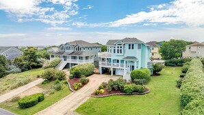 Uma casa grande e azul clara com um amplo jardim frontal e uma entrada com acesso por um caminho.