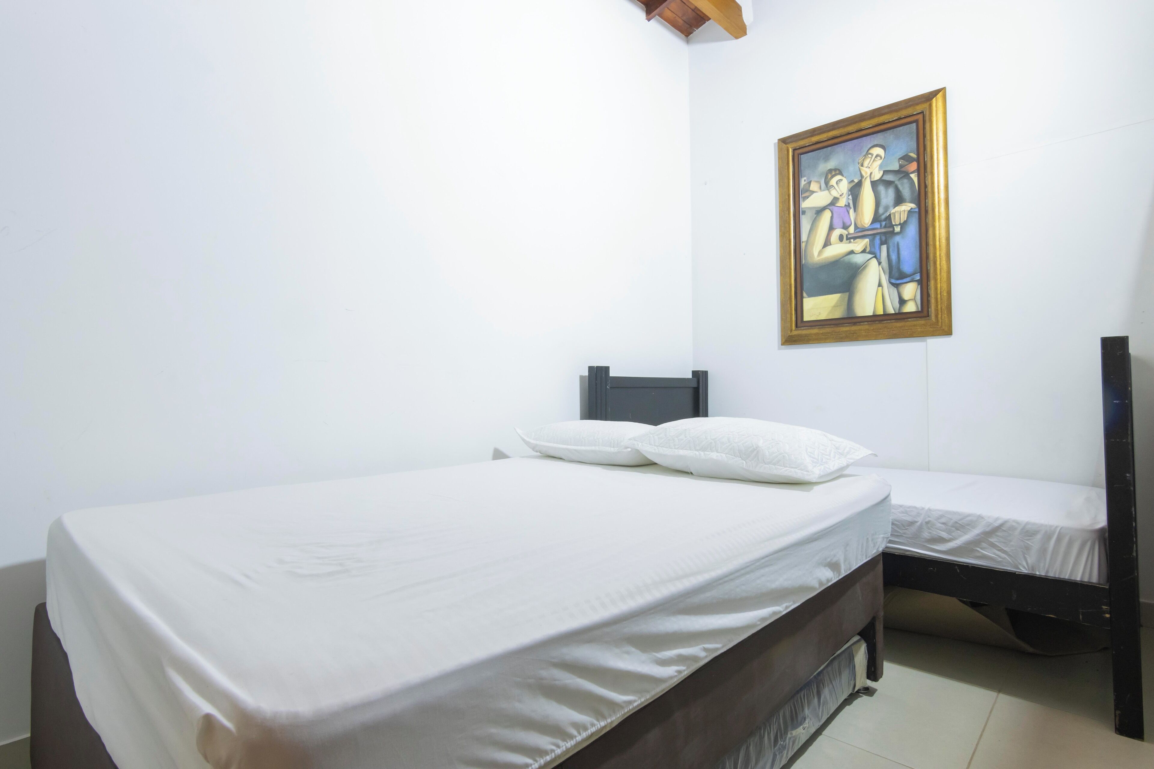 Une chambre avec un lit simple, une petite table de chevet, une commode et un tableau au mur.