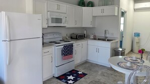 A modern kitchen with white cabinetry, a refrigerator, a microwave, a stove, and a sink. There is a small dining area with a table and chairs. - Charming 1-bedroom apartment with WiFi and AC in delightful Port Charlotte (Port Charlotte)