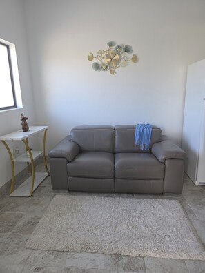 Relax in this stylish living room with a grey sofa, side table, and decorative clock, surrounded by a large window and soft rug.