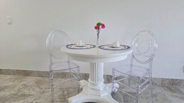 A round white table with two clear plastic chairs, a vase with flowers, and a decorative plate. - Charming 1-bedroom apartment with WiFi and AC in delightful Port Charlotte (Port Charlotte)
