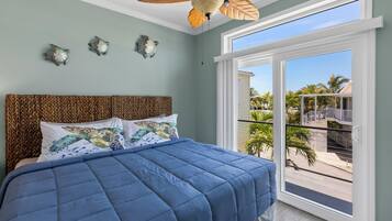 Een slaapkamer met een groot bed, een plafondventilator en uitzicht op een balkon met palmbomen.