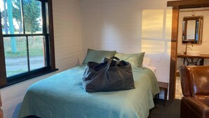Um quarto com uma cama, janela, espelho e cadeira.