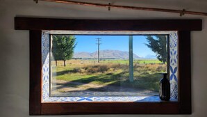Uma janela com vista para um campo gramado, uma árvore e montanhas ao longe.